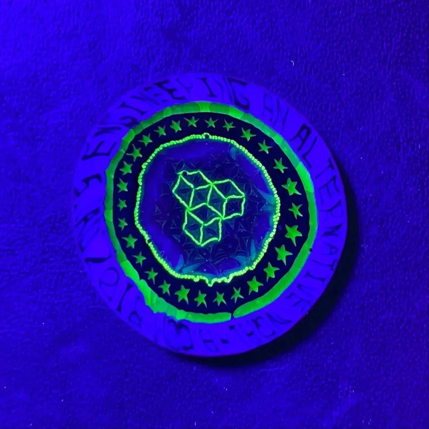 UV-reactive glass art disc with geometric and star patterns glowing under blacklight