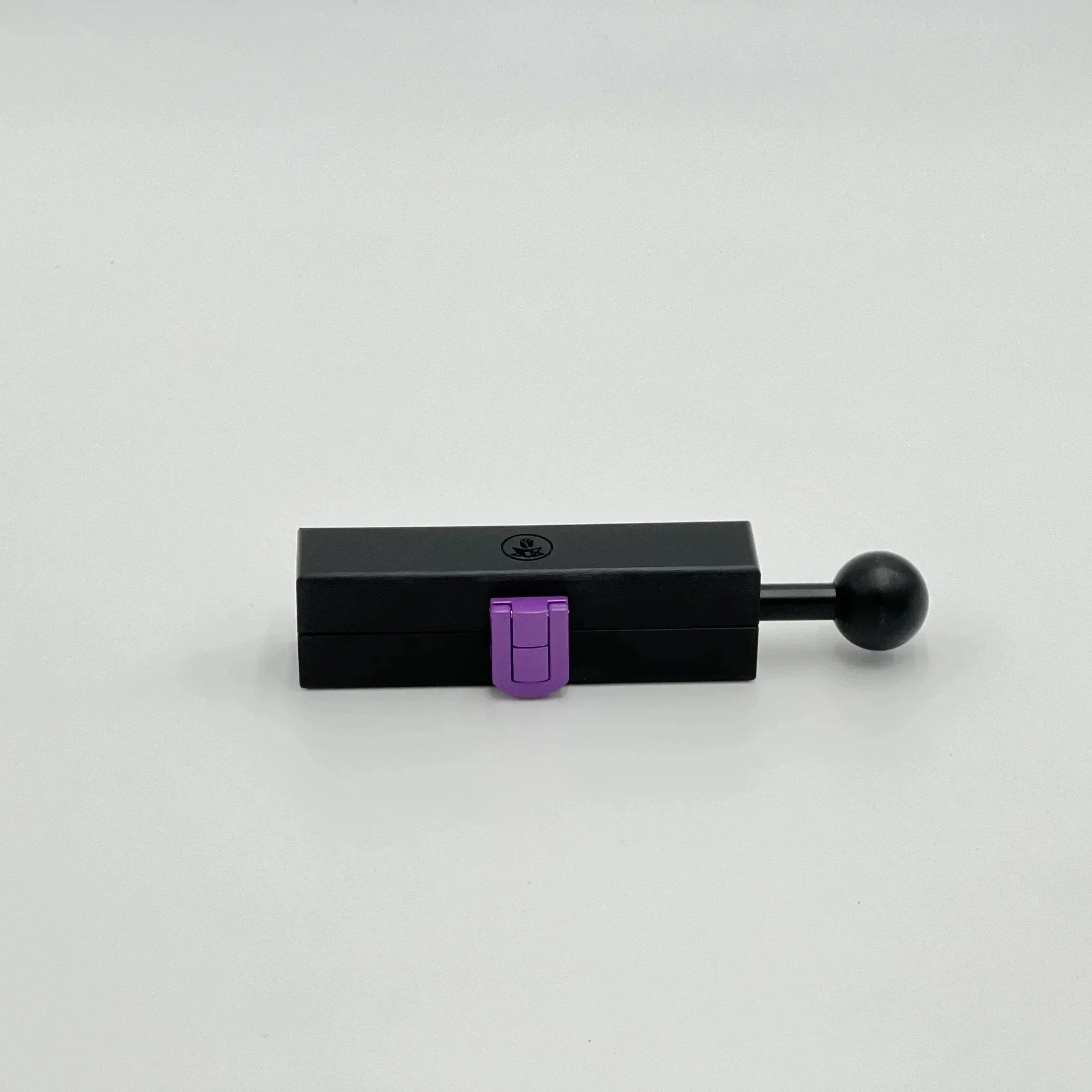 Black rectangular herb grinder with purple latch and round handle on white background