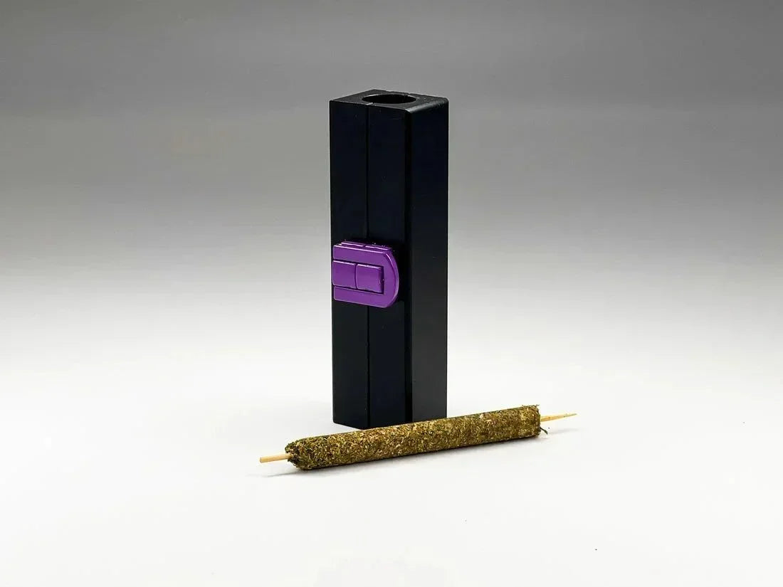 Herb and tobacco rolling tool with purple button and a finished pre-roll on a gray background