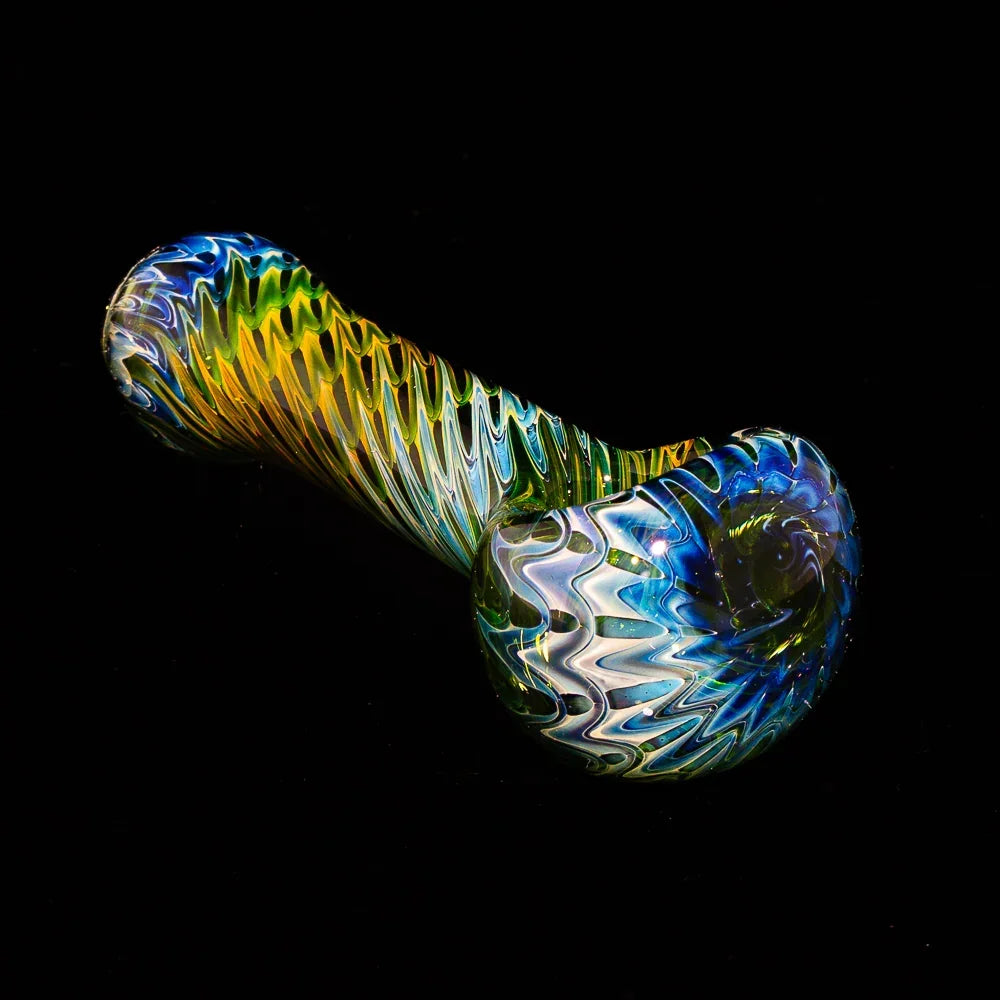 Handblown glass spoon pipe with green, blue, and yellow raked fume design on black background