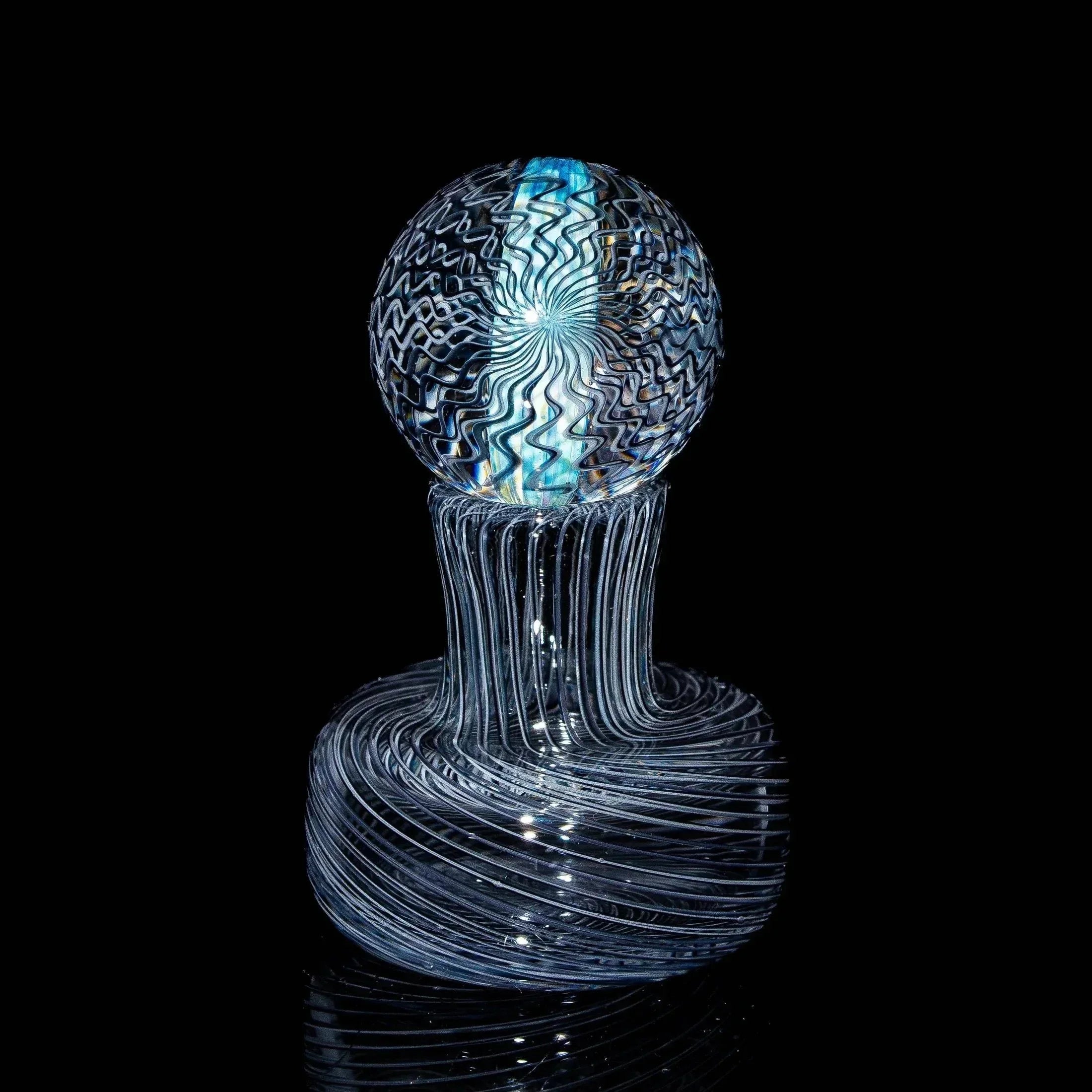 Handblown glass marble with intricate blue and white swirl patterns on black background