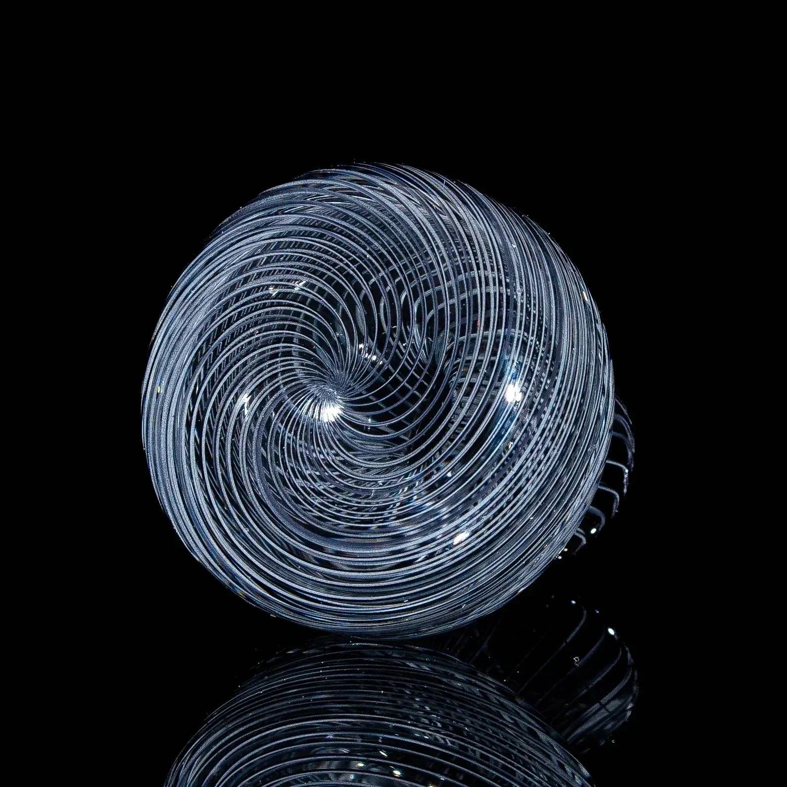 Clear glass marble with intricate spiral pattern on black reflective surface