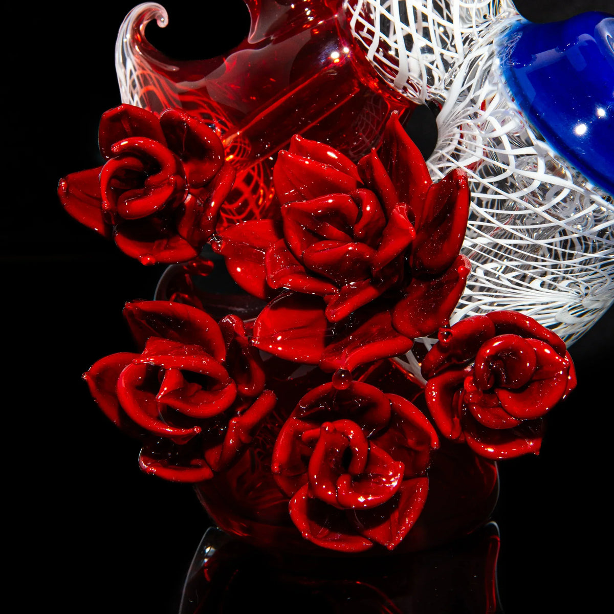 Close-up of intricate red glass roses on an artistic glass water pipe with white and blue accents.