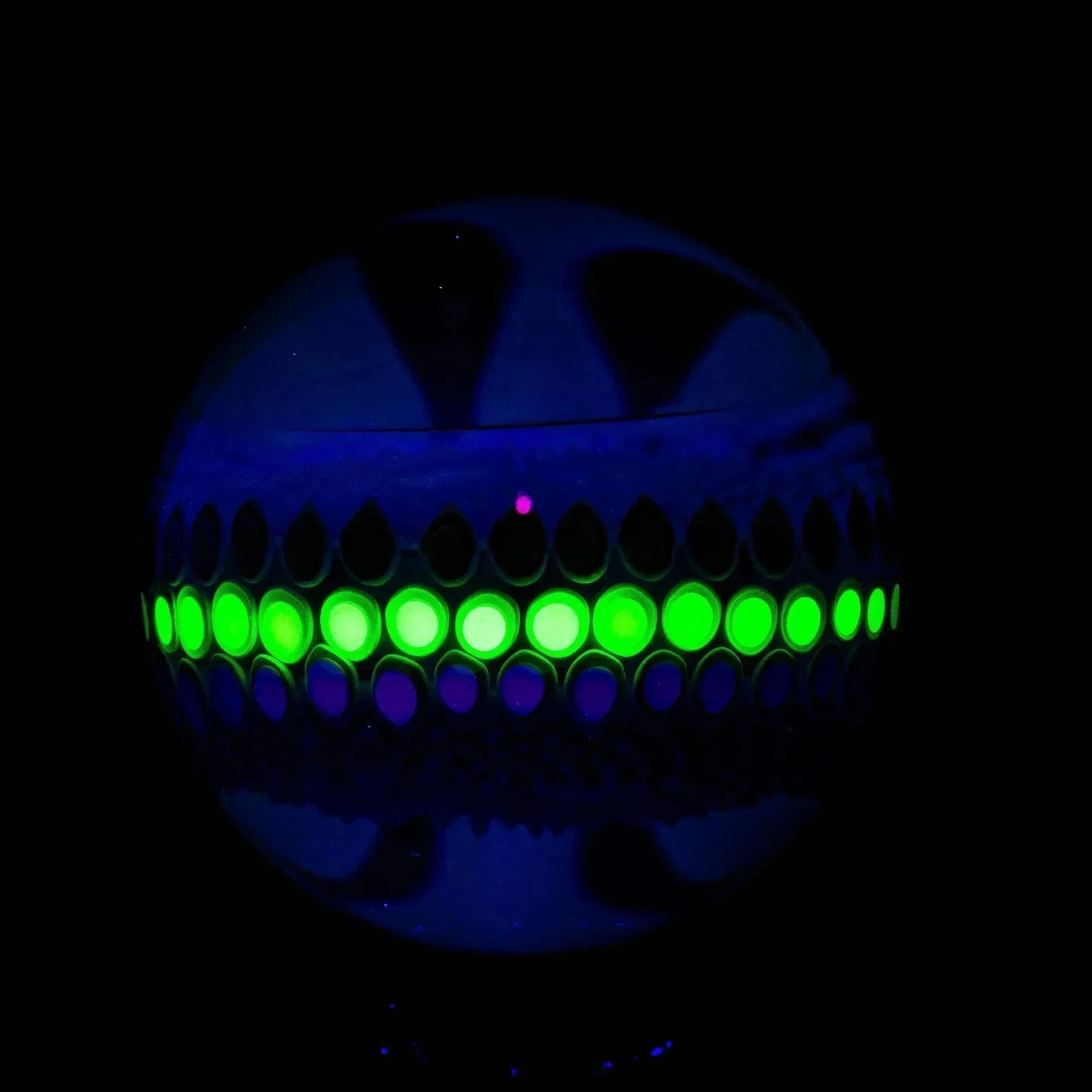 UV reactive glass marble with glowing green and purple dot pattern on black background
