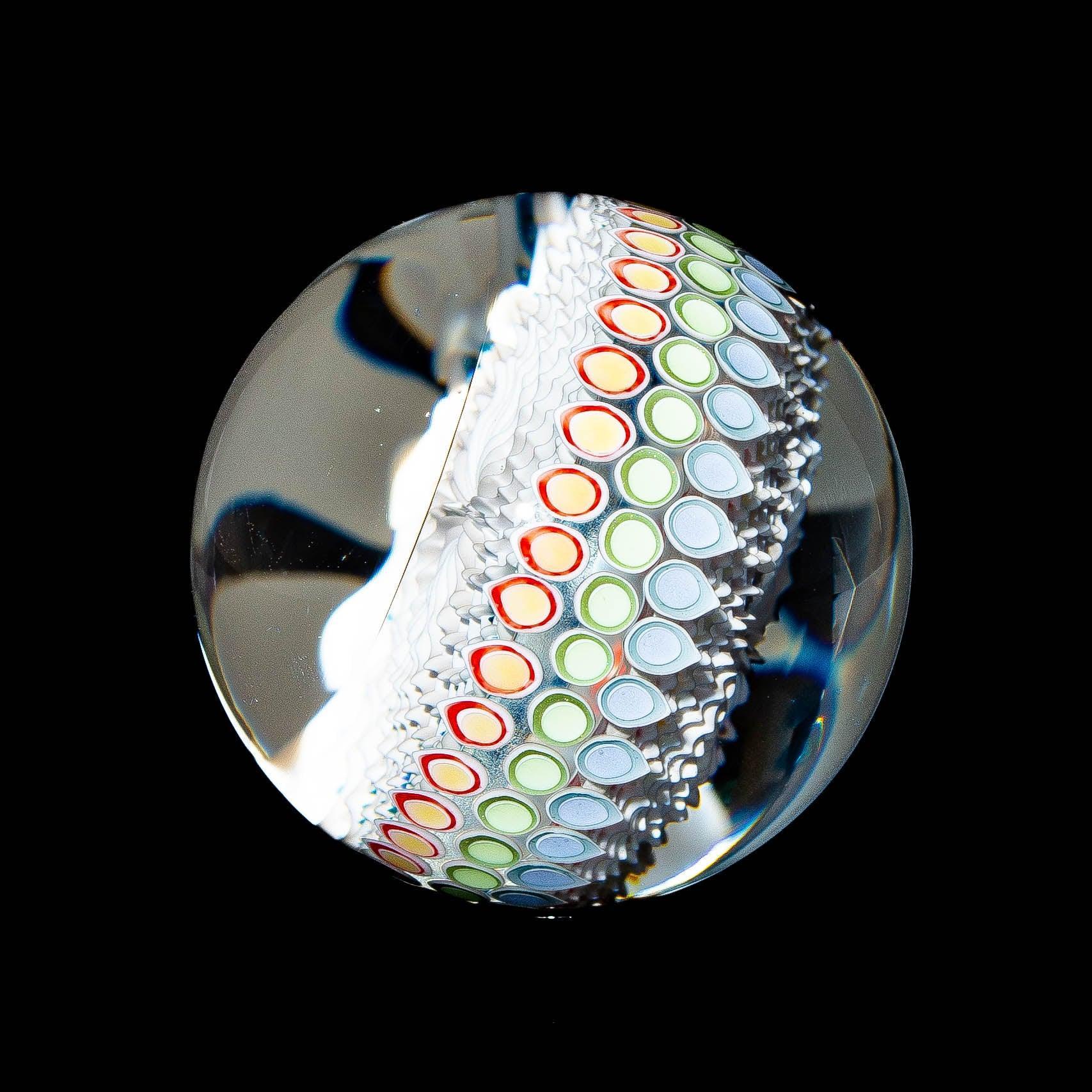 Handcrafted glass marble with colorful dot stack design on black background