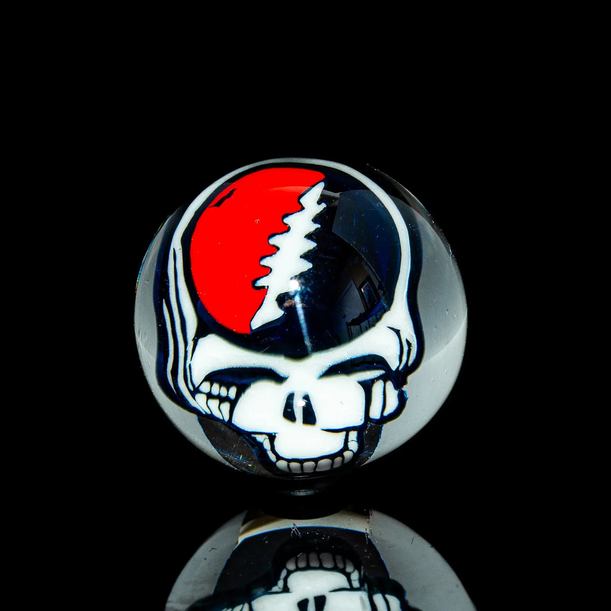 Handcrafted glass marble featuring a skull with a red and blue design on black background