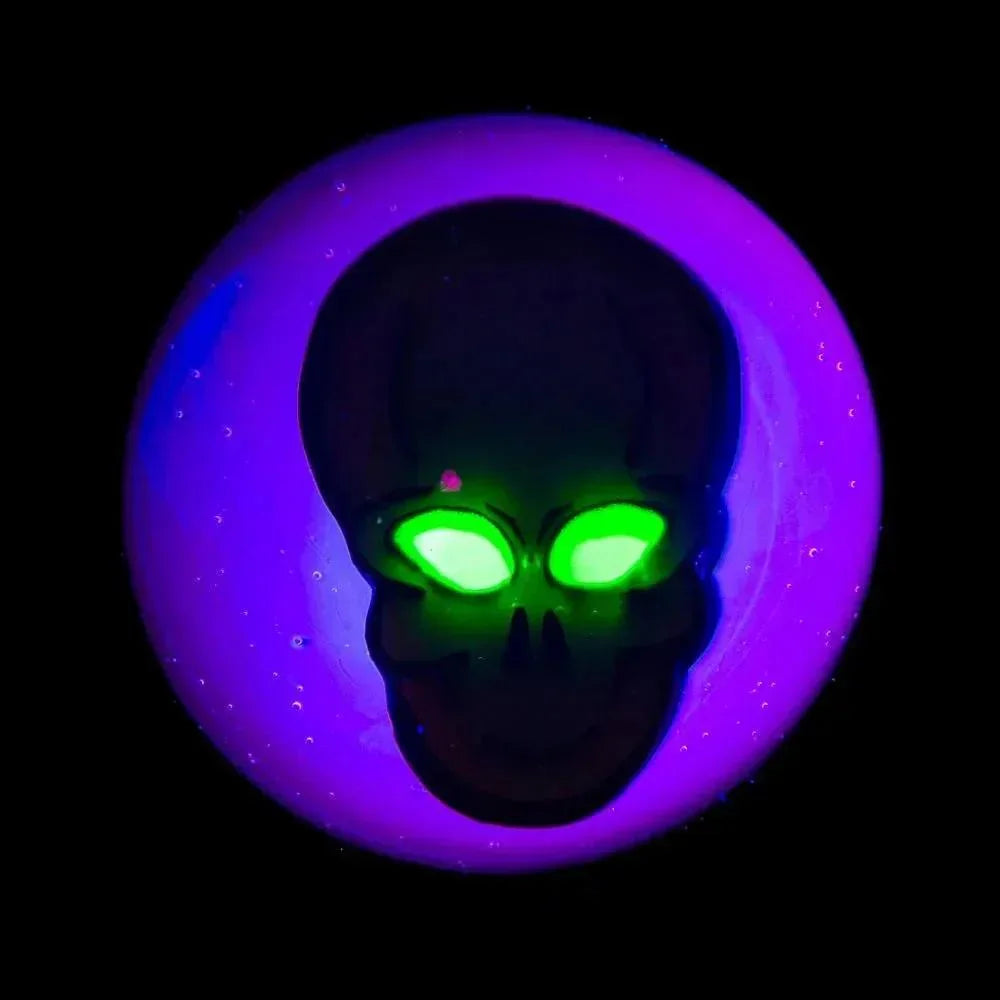 UV-reactive glass marble with glowing green alien skull design on a purple background