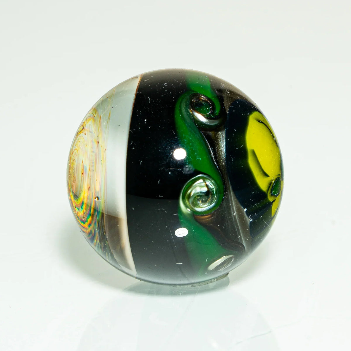 Heady glass marble with rainbow dichroic vortex, green swirls, and yellow accents on white background