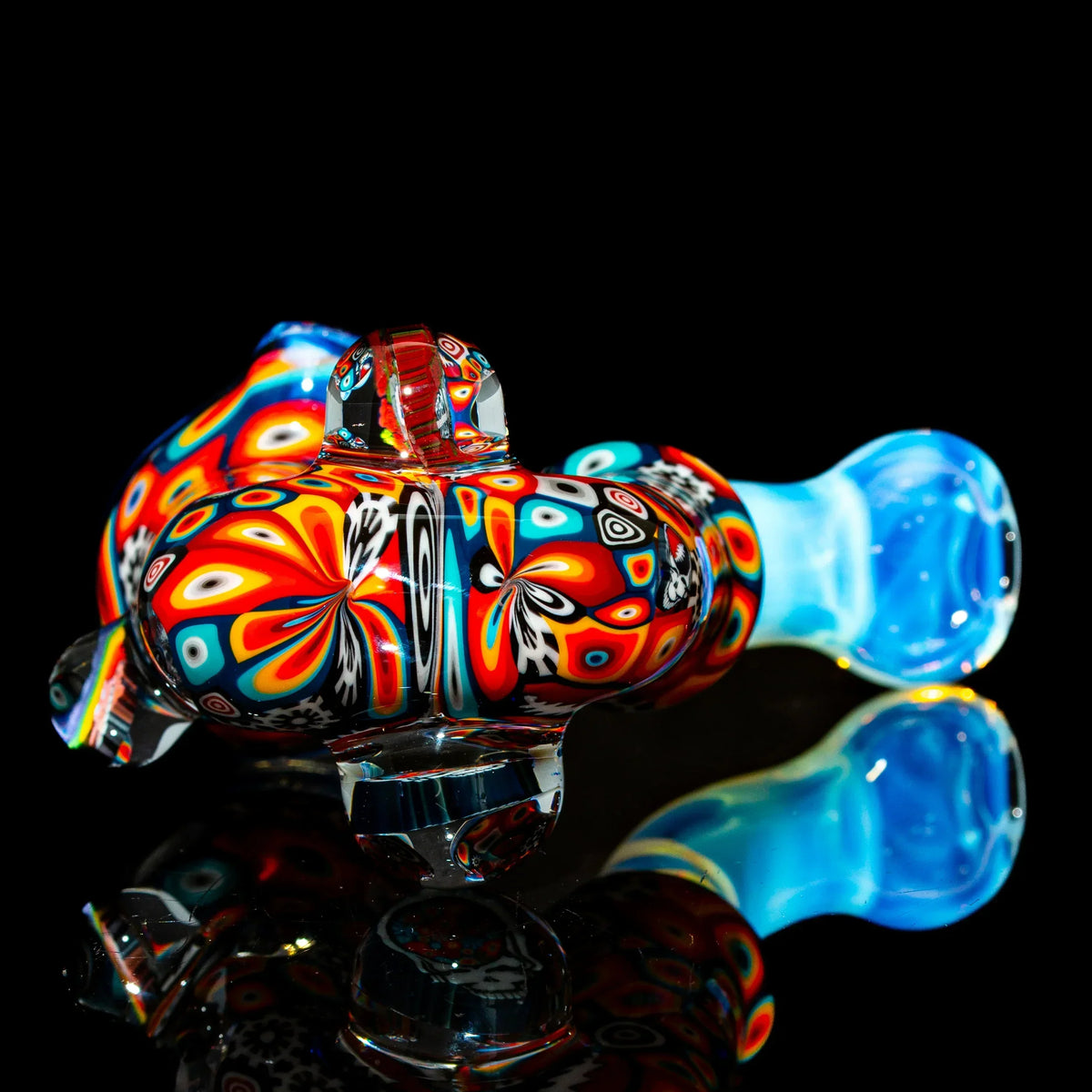 Colorful hand-blown glass pipe with intricate patterns on a reflective black surface