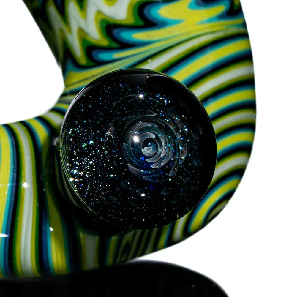 Close-up of a glass pipe with green, yellow, and black swirled linework and a sparkling marble accent.