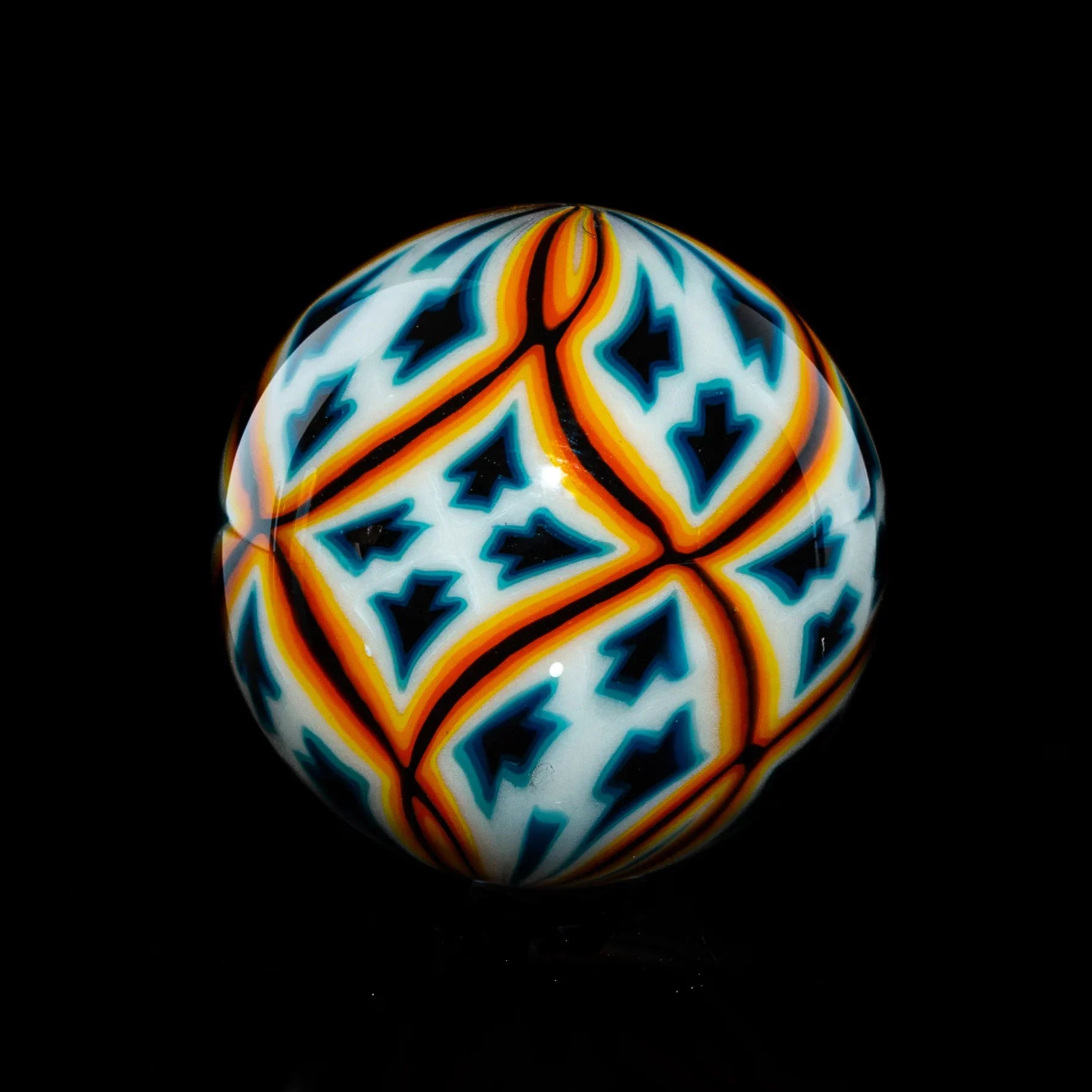 Handcrafted glass marble with geometric blue, orange, and white pattern on black background