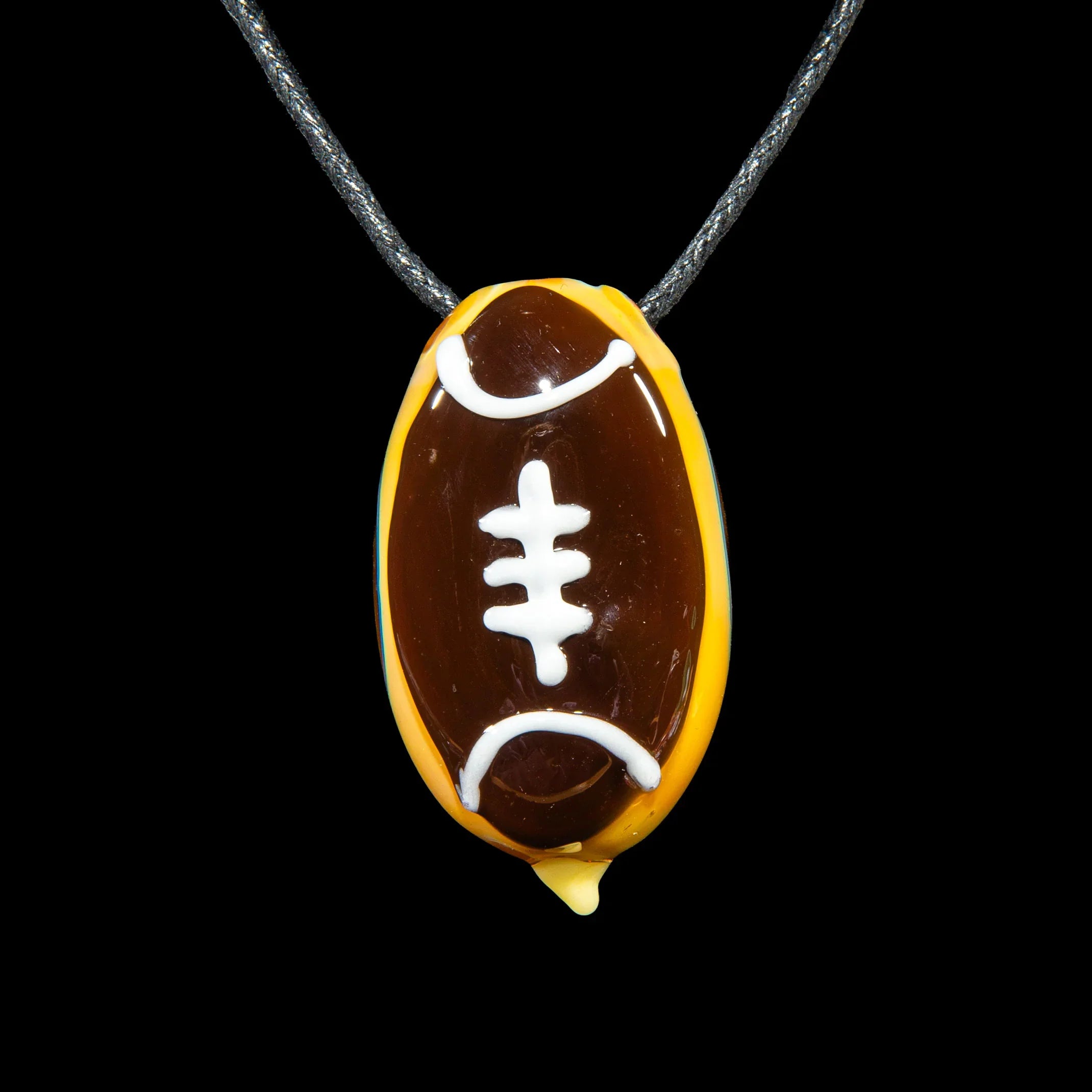 Glass pendant shaped like a football on a cord necklace, brown and yellow with white laces.