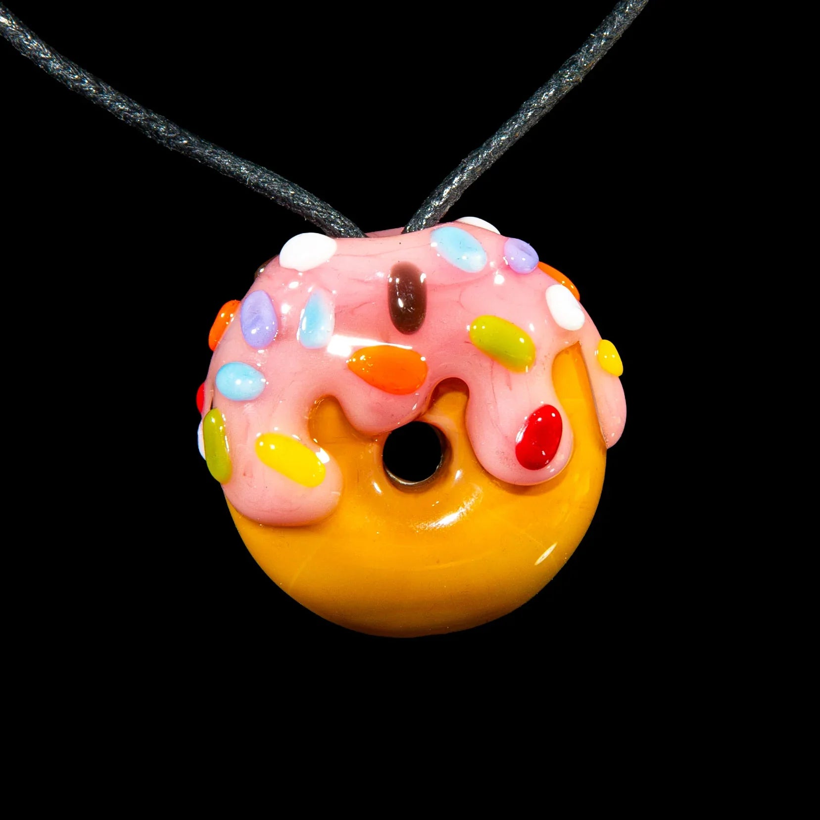 Glass donut pendant with pink frosting and rainbow sprinkles on a cord necklace