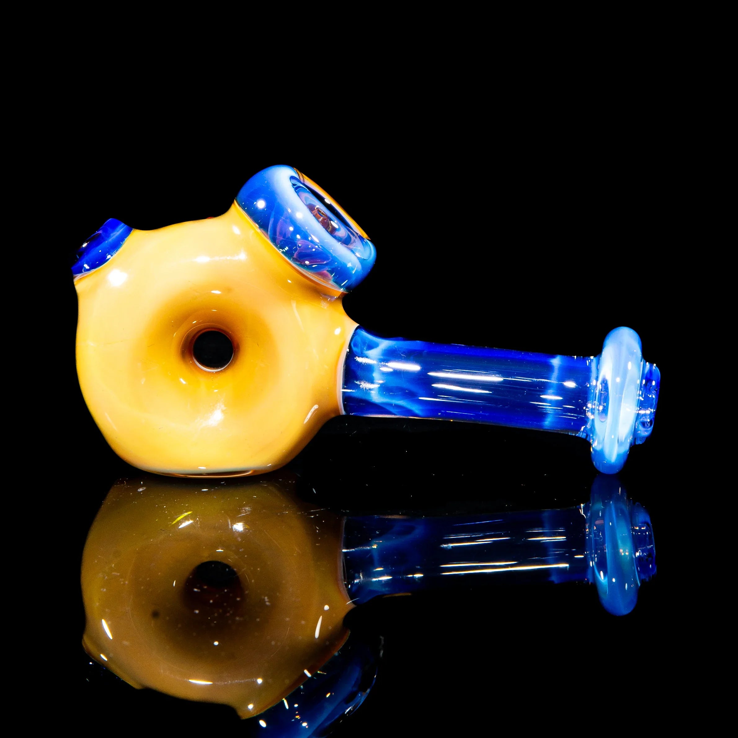 Blue and yellow glass hammer pipe with donut-shaped chamber on a black reflective surface