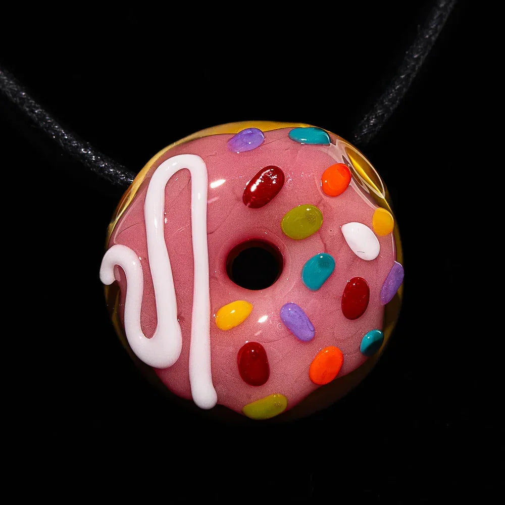 Glass donut pendant with pink frosting, sprinkles, and white drizzle on a black cord