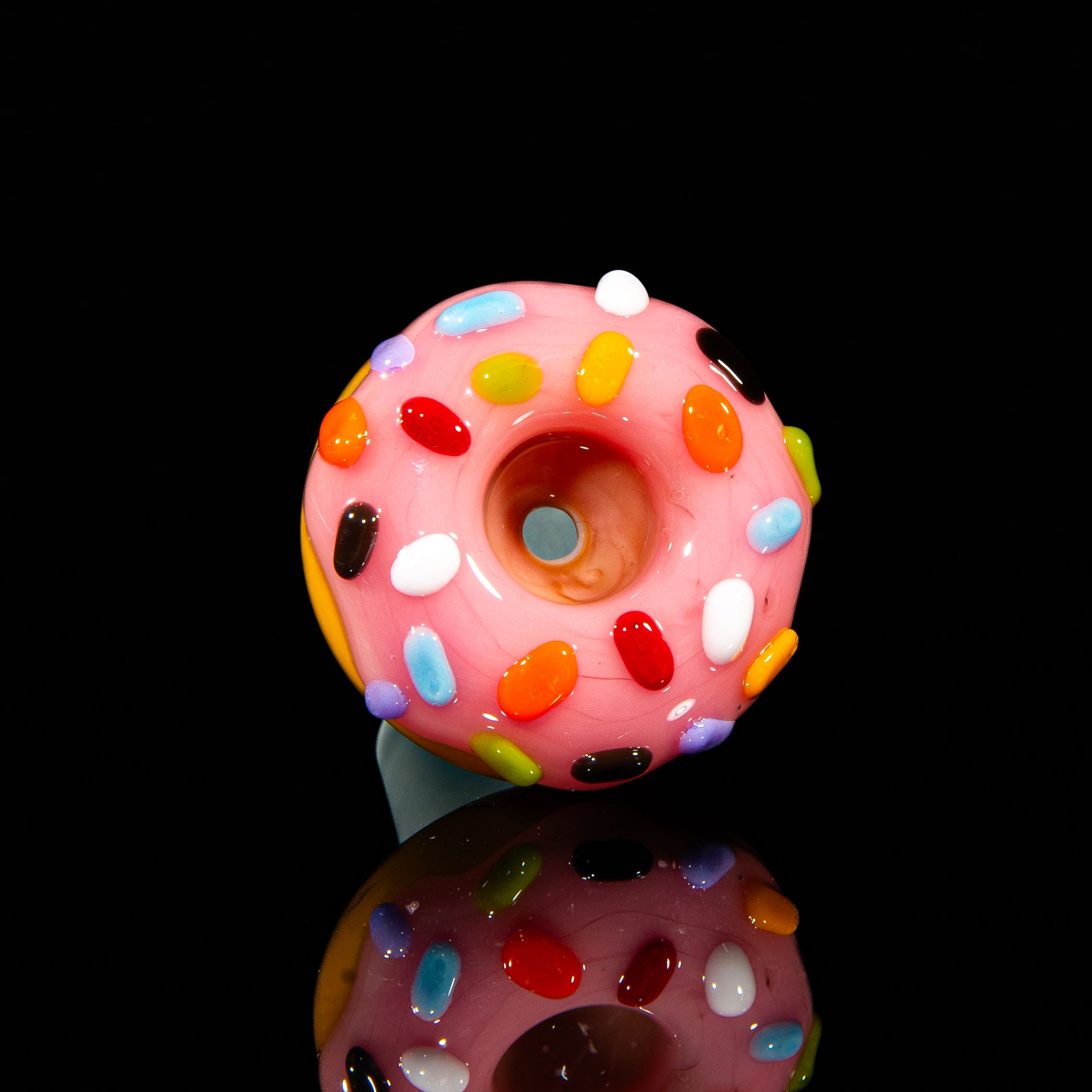 Pink glass slide shaped like a donut with colorful sprinkles, on a black background.