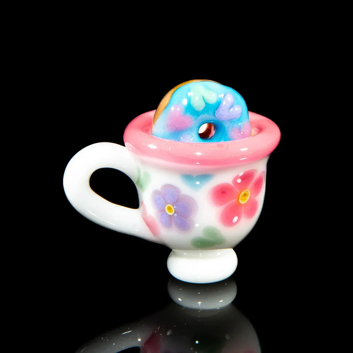 Glass pendant shaped like a pink floral teacup with a blue donut inside, on black background