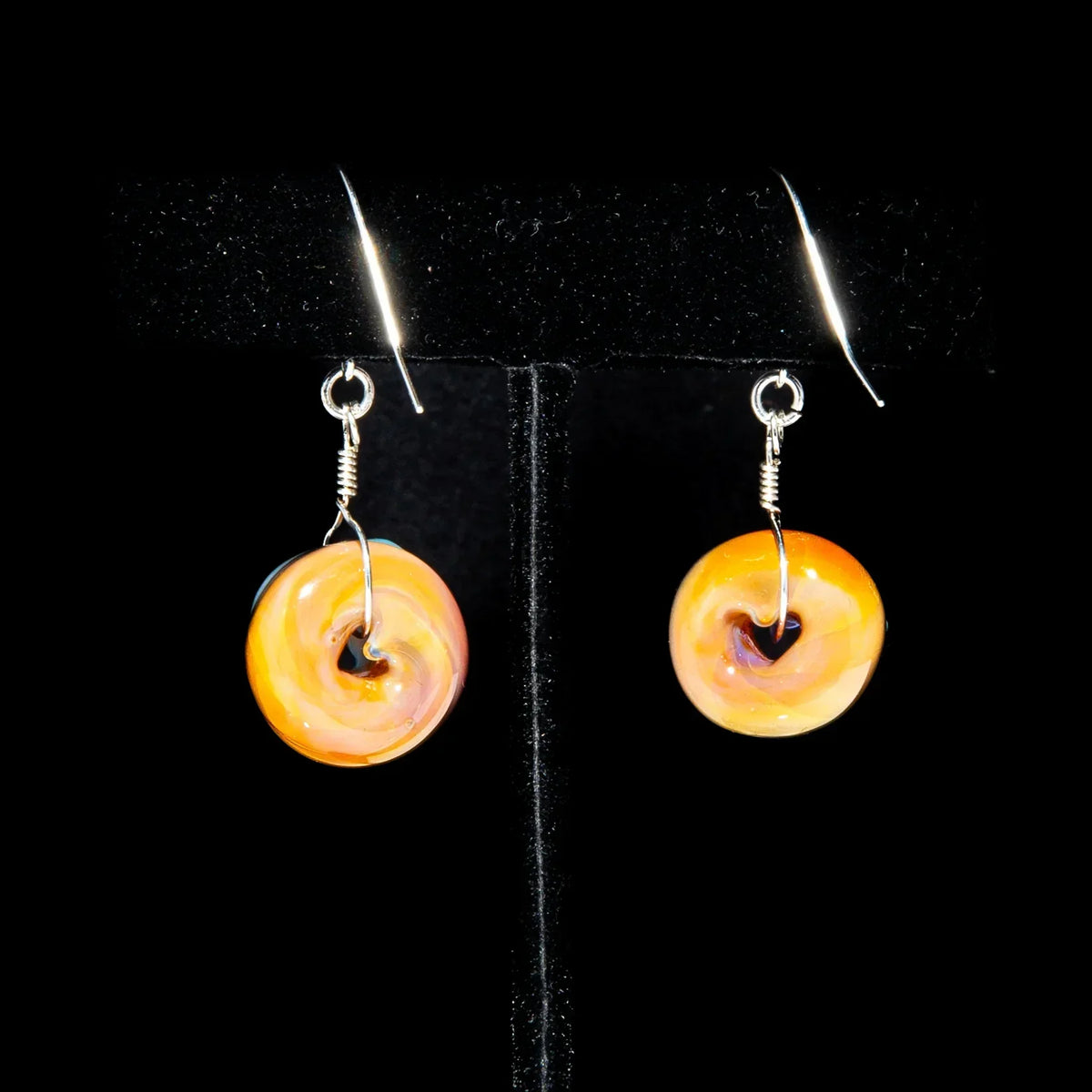 Handmade glass donut earrings with orange and yellow swirls on silver hooks