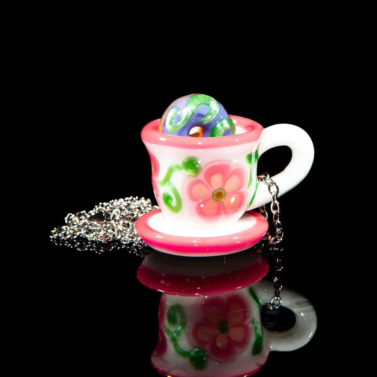 Glass pink floral teacup pendant with chain and colorful marble on black background