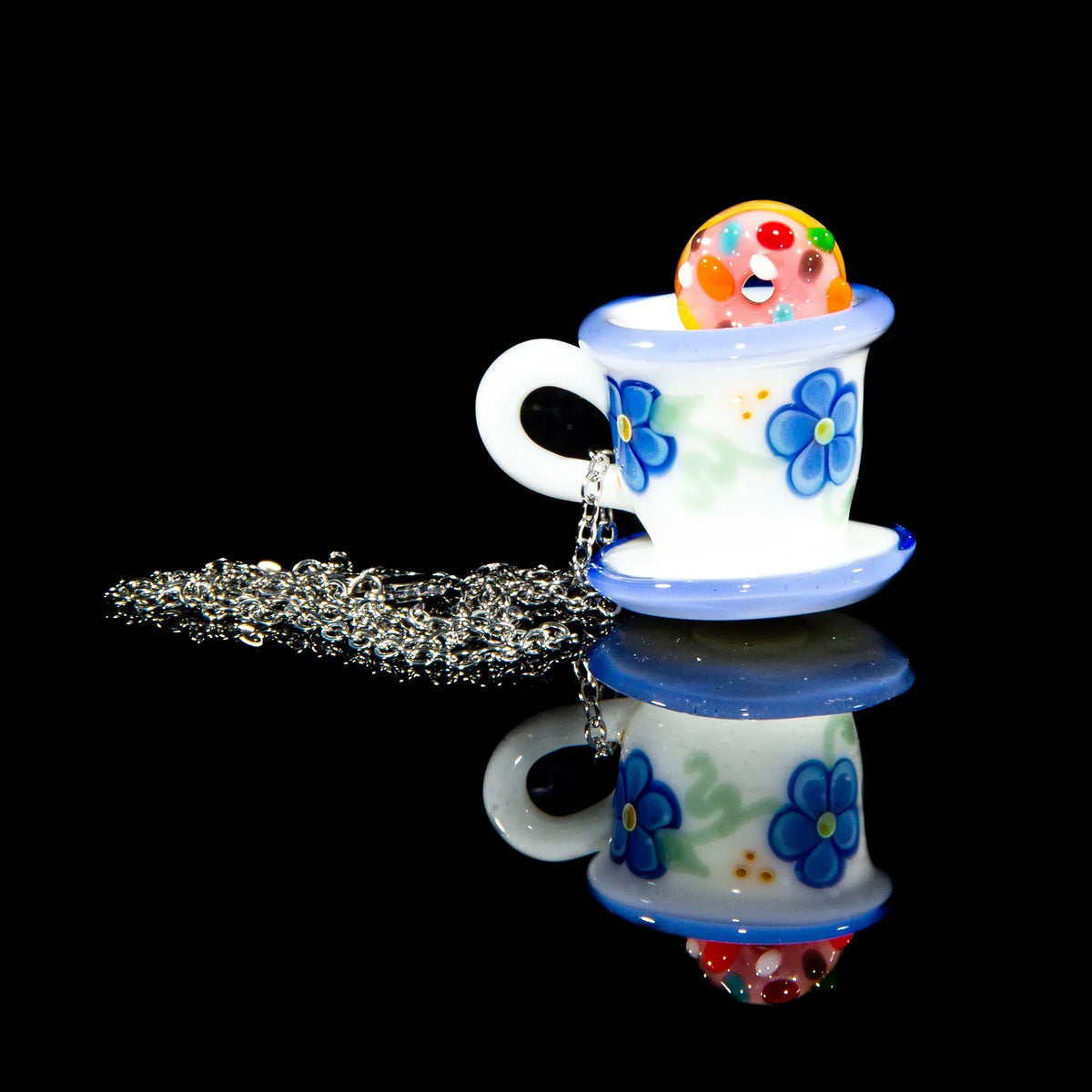 Glass pendant necklace shaped like a blue floral teacup with a colorful donut charm