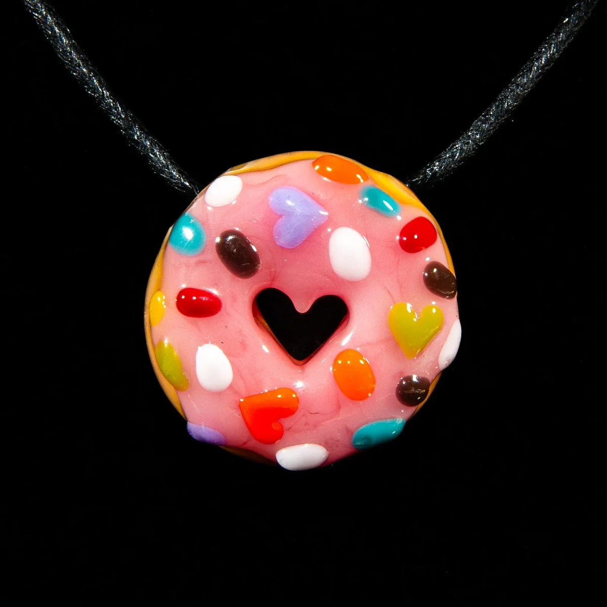 Pink glass donut pendant with rainbow heart sprinkles and heart-shaped center on a cord