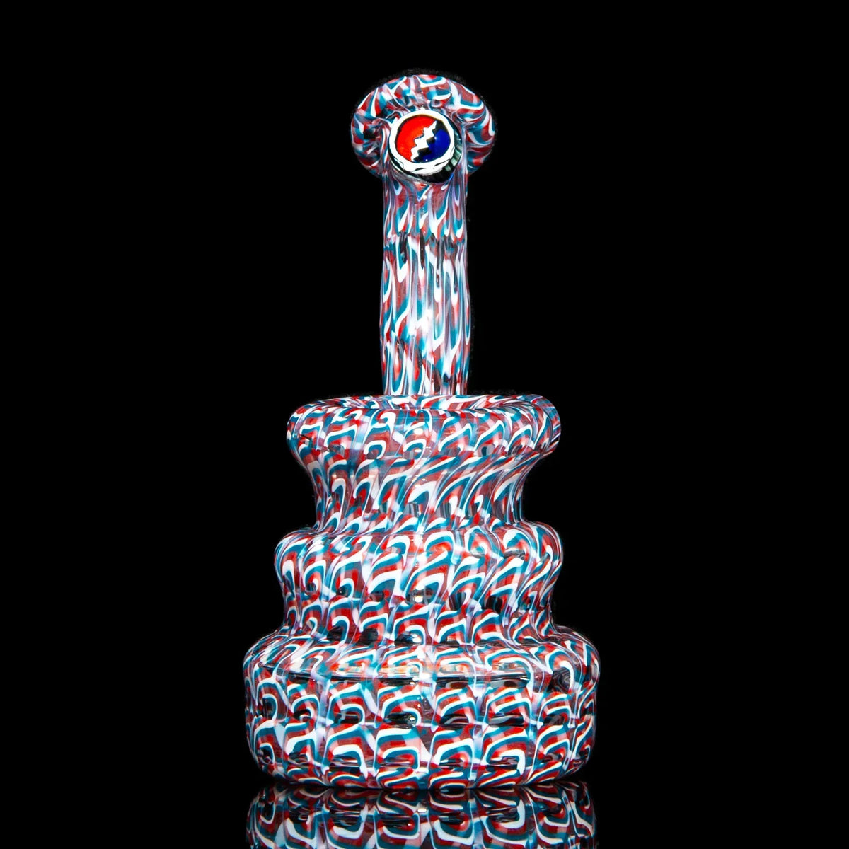 Heady glass water pipe with red, white, and blue pattern, round tiered base on black background