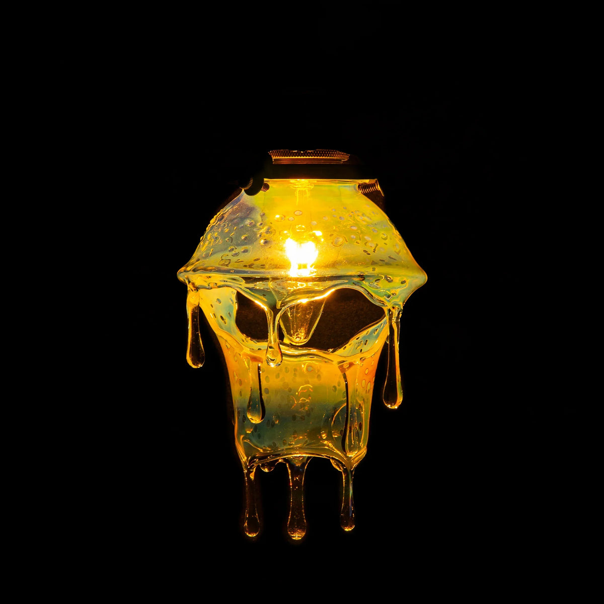Hand-blown glass lamp with skull design and dripping effect, illuminated against black background