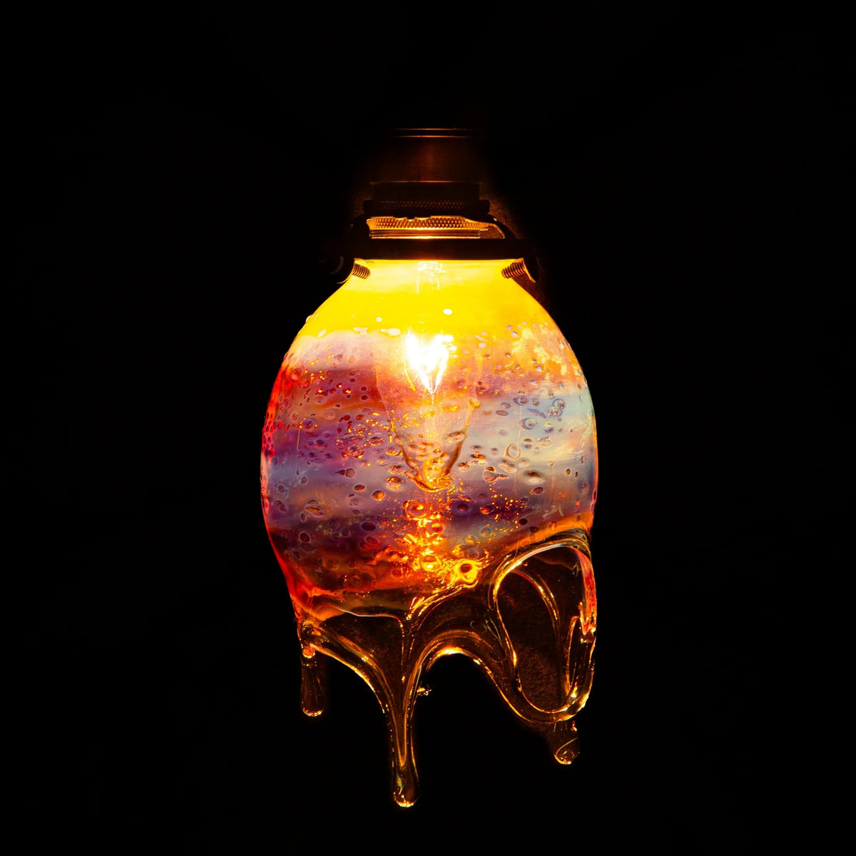 Colorful glass pendant lamp with molten drip design, glowing against a dark background