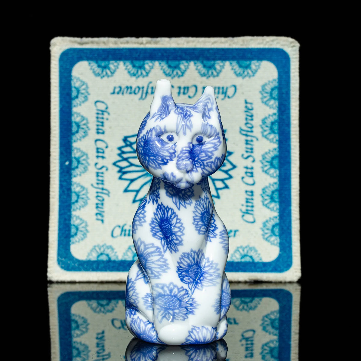 Porcelain cat figurine with blue sunflower pattern, seated in front of matching mat