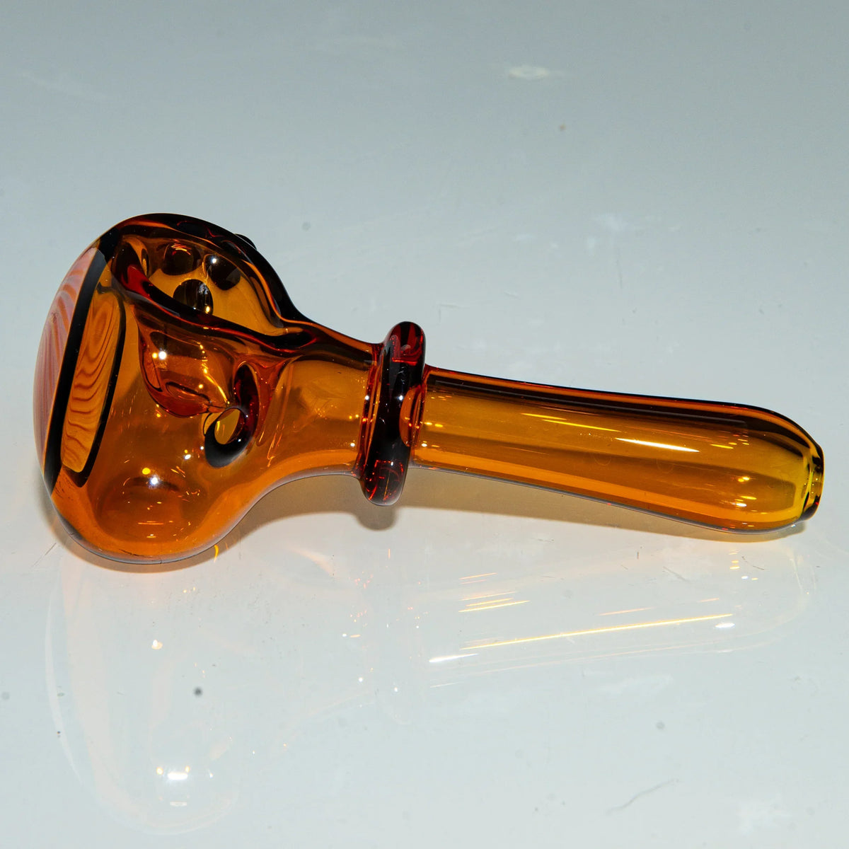 Amber glass hand pipe with black dot accents on a white background