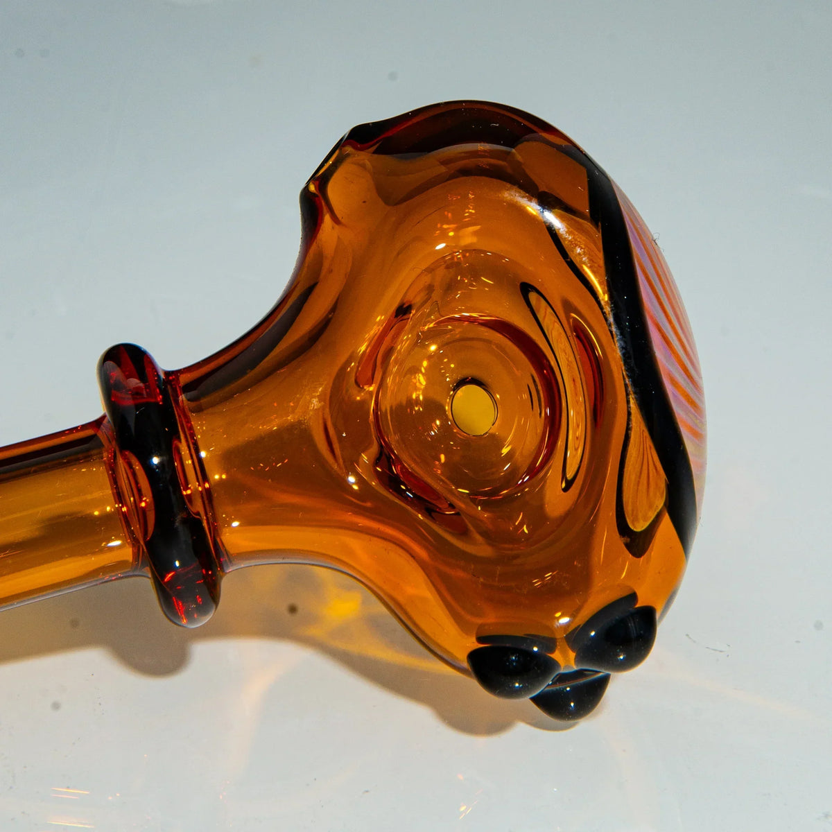 Amber glass hand pipe with black accents and a portal-style bowl on white background