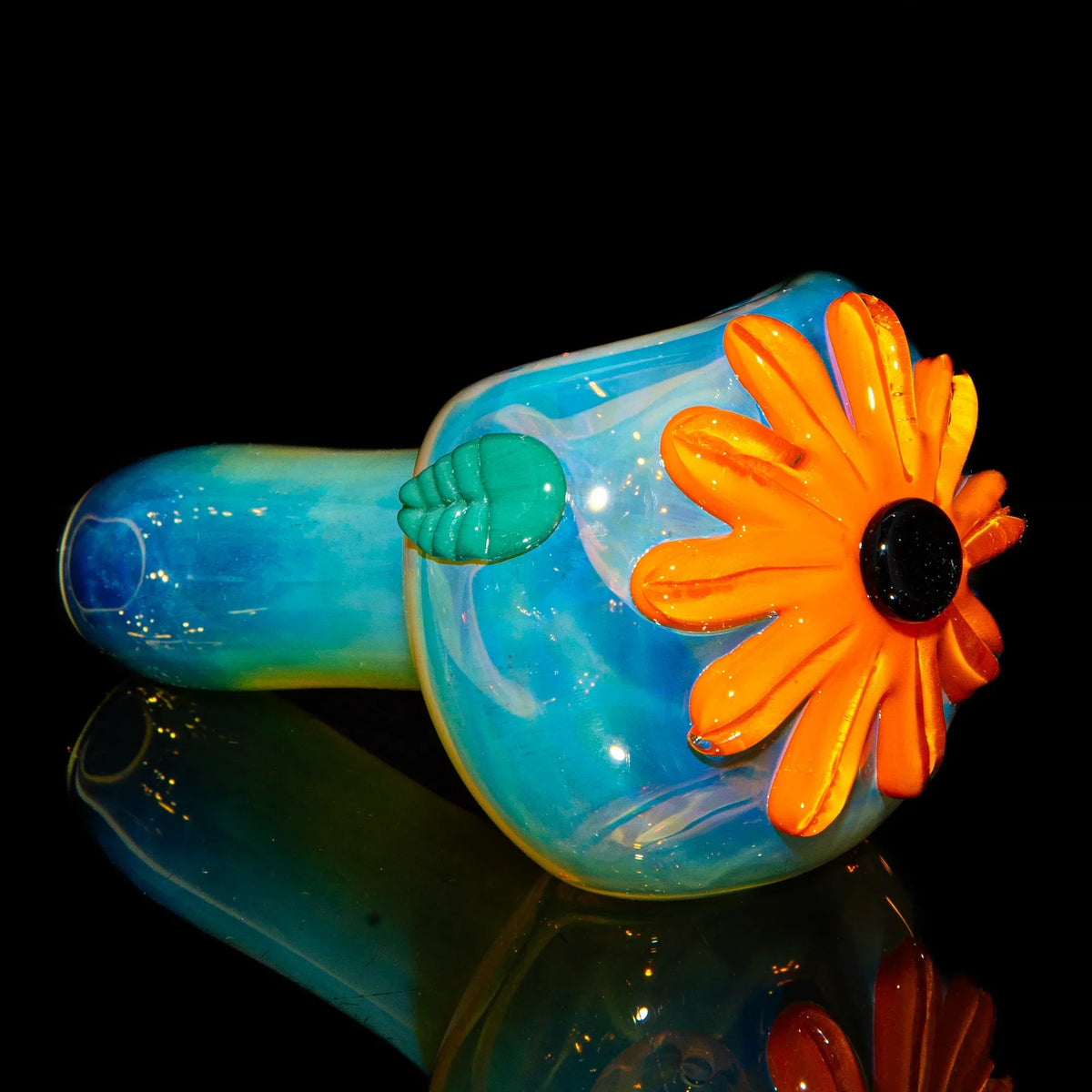 Blue glass hand pipe with orange flower and green leaf accent on black background