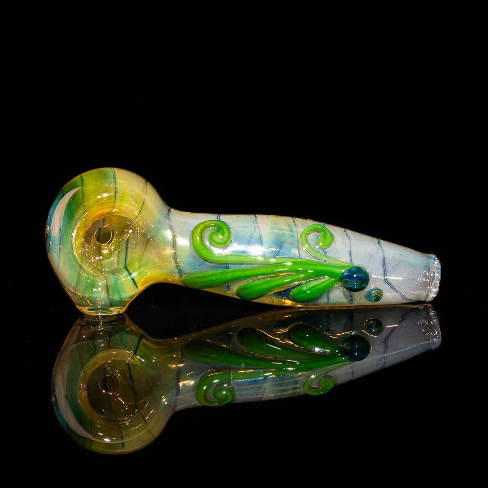 Hand-blown glass spoon pipe with green flower design on a reflective black background