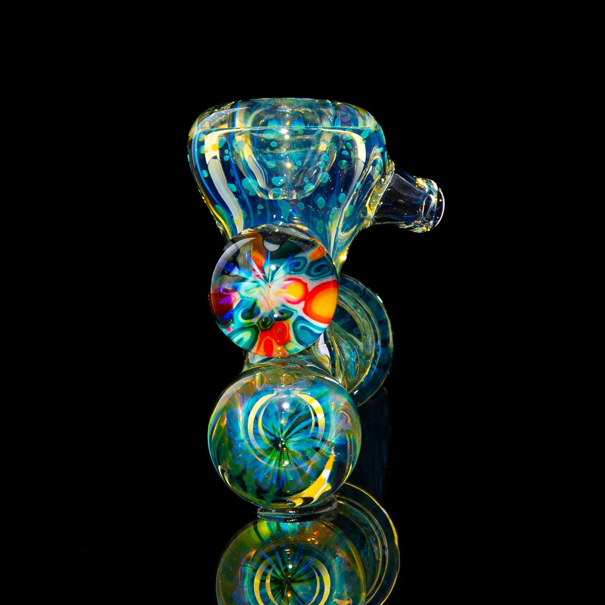 Colorful glass pipe with intricate patterns and marbles on a black reflective surface