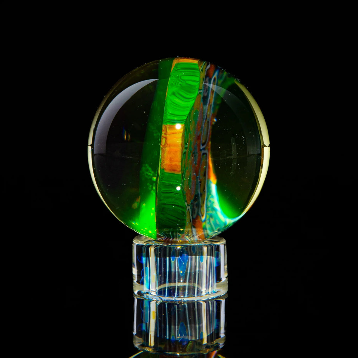 Handcrafted glass marble with green and orange patterns on a clear stand, art glass photography