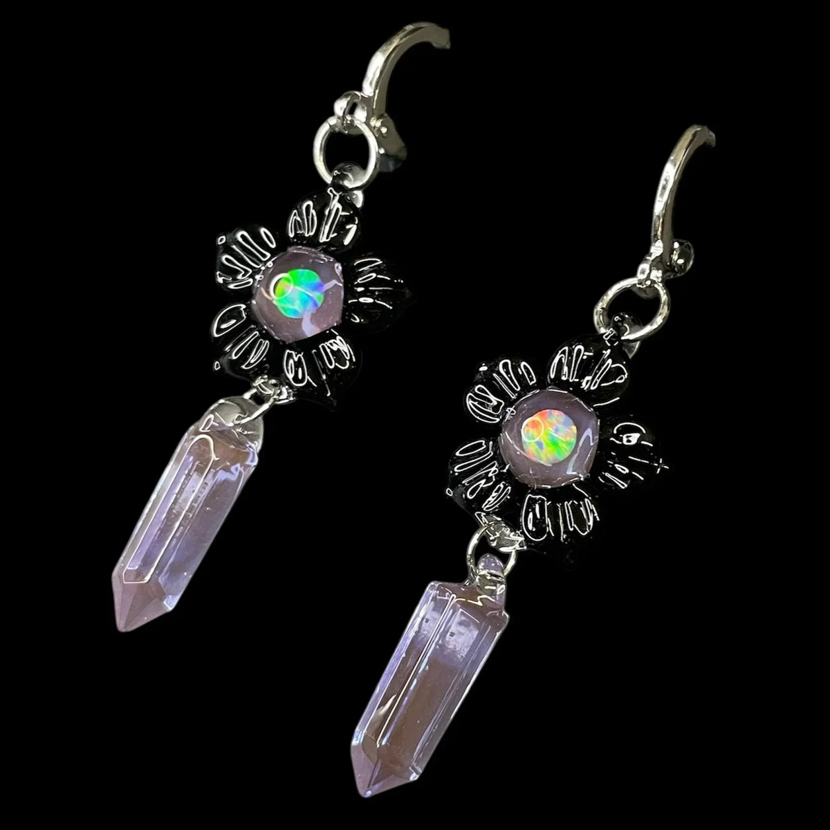 Crystal point earrings with iridescent gemstone center and metallic floral design on black background.