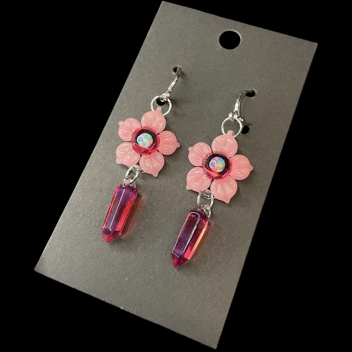 Pink flower earrings with iridescent center and magenta crystal point dangles on display card