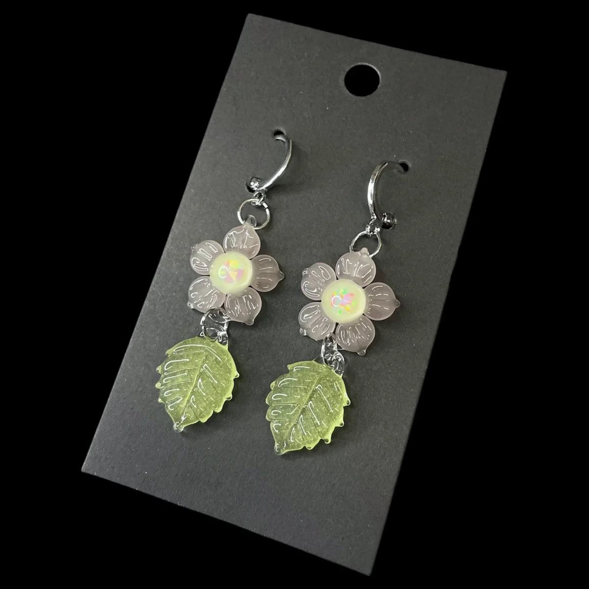 Handmade glass earrings with clear flower and green leaf charms on black card display.
