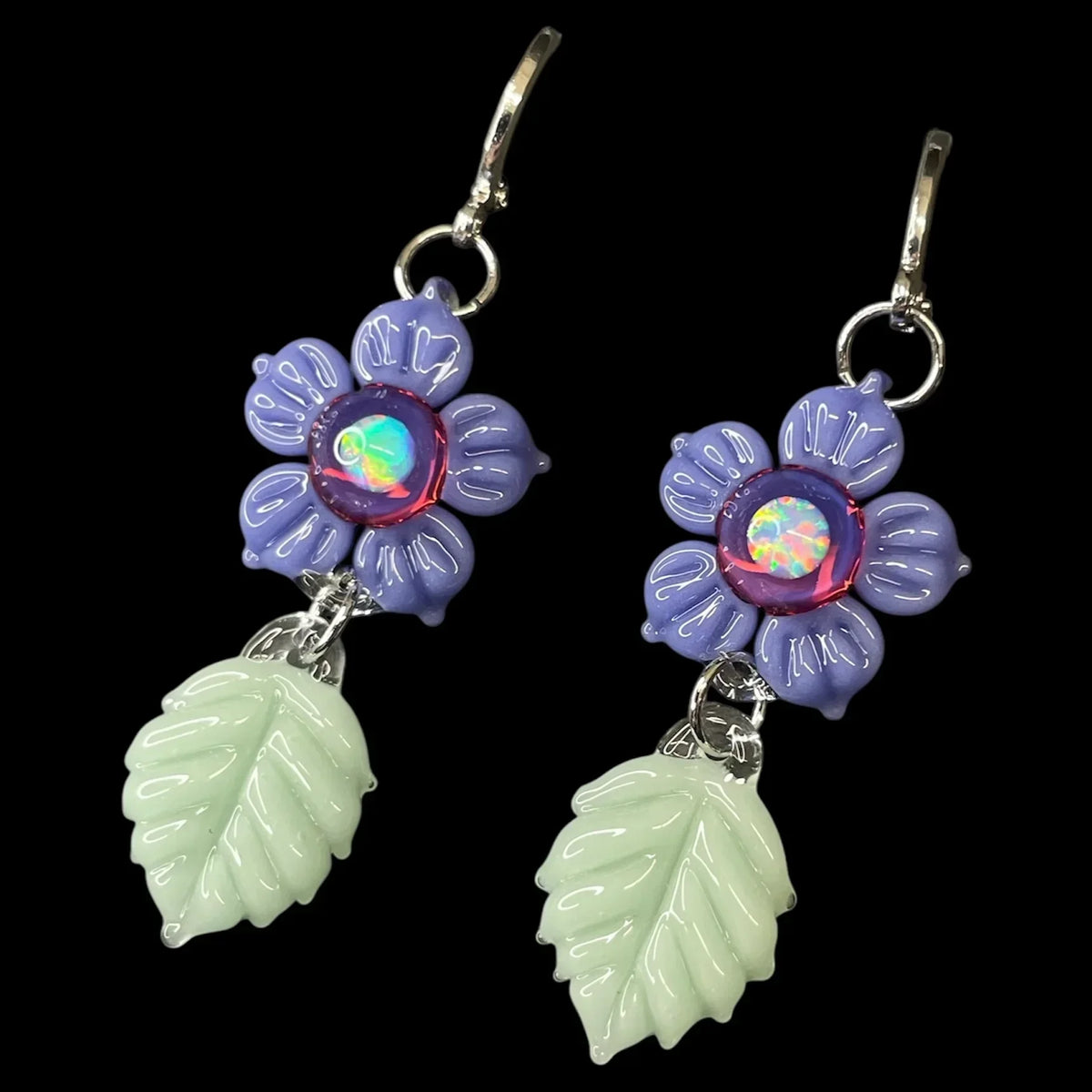 Handcrafted glass earrings with purple flower and green leaf design on black background