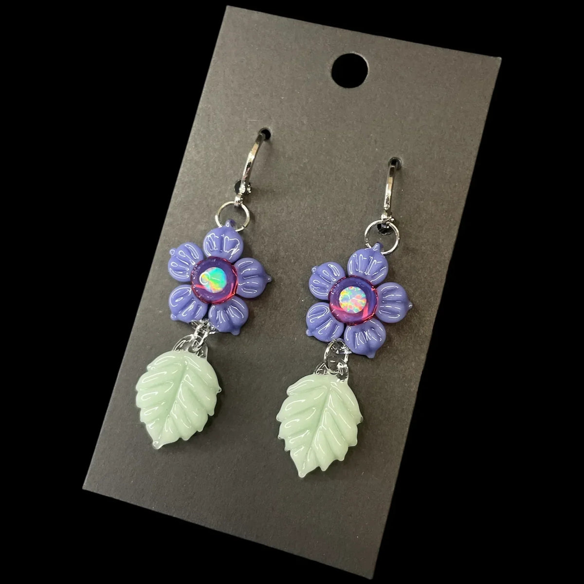 Handmade glass earrings with purple flower and light green leaf charms on display card