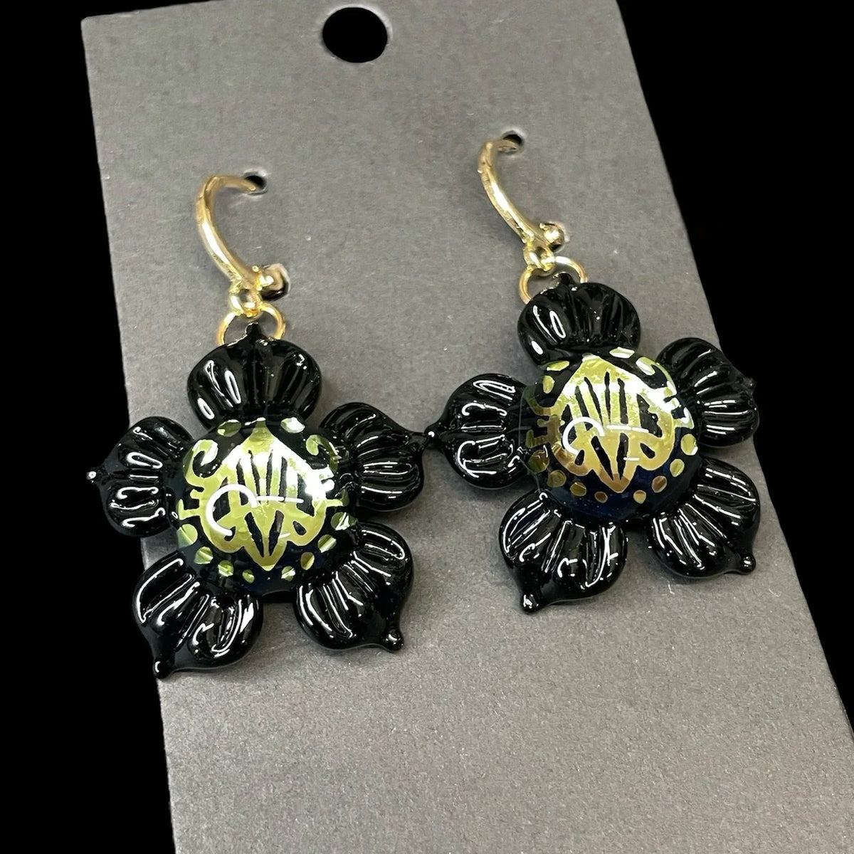 Black glass flower earrings with gold accents and hooks displayed on a gray card