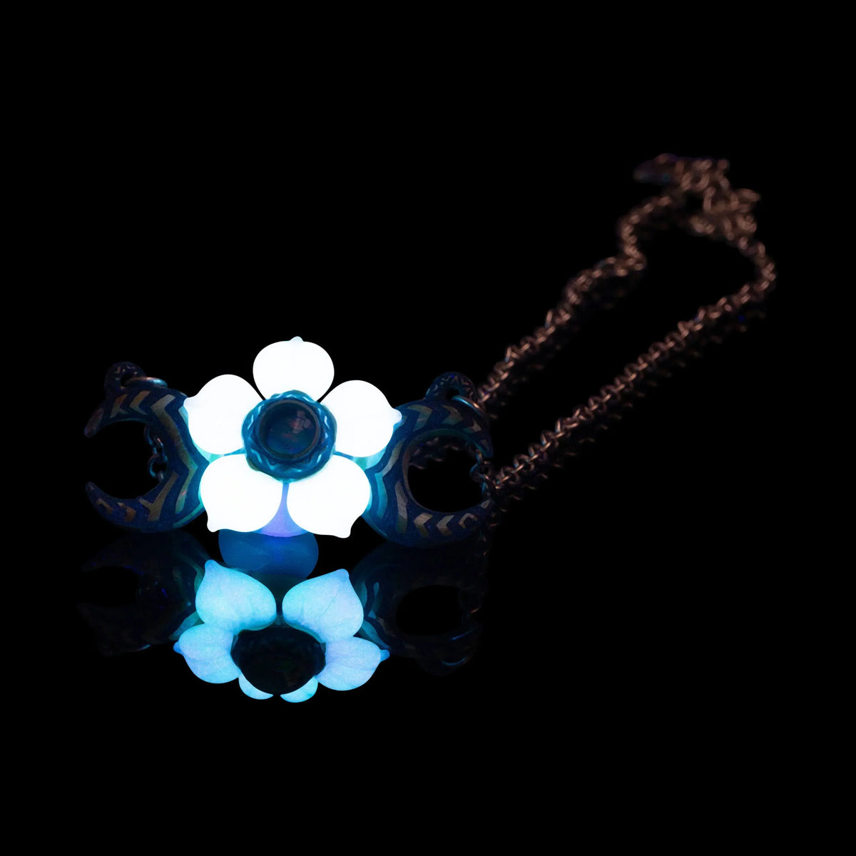 Handcrafted glass pendant necklace with glowing white flower and crescent moons on black background