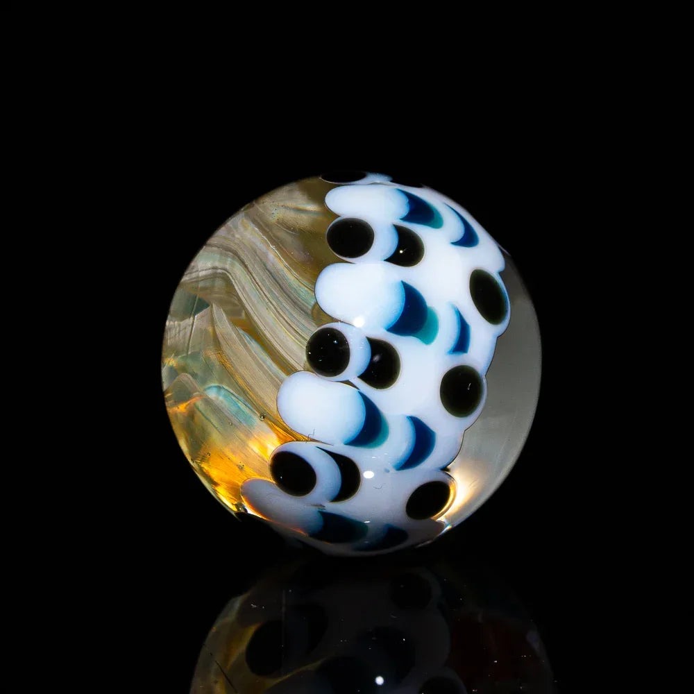 Handcrafted glass marble with blue, white, and black dot pattern on a swirling gold background