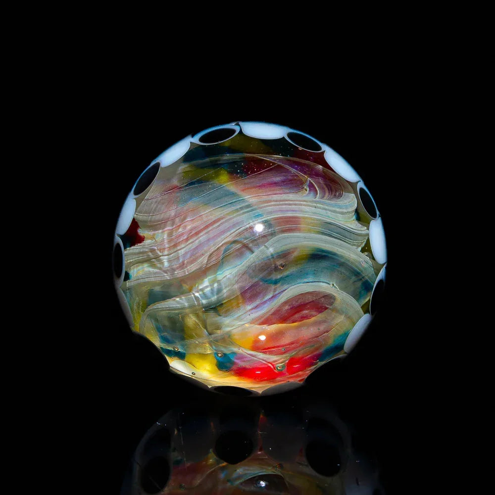 Handcrafted heady glass marble with colorful swirls and black and white dot rim on black background.