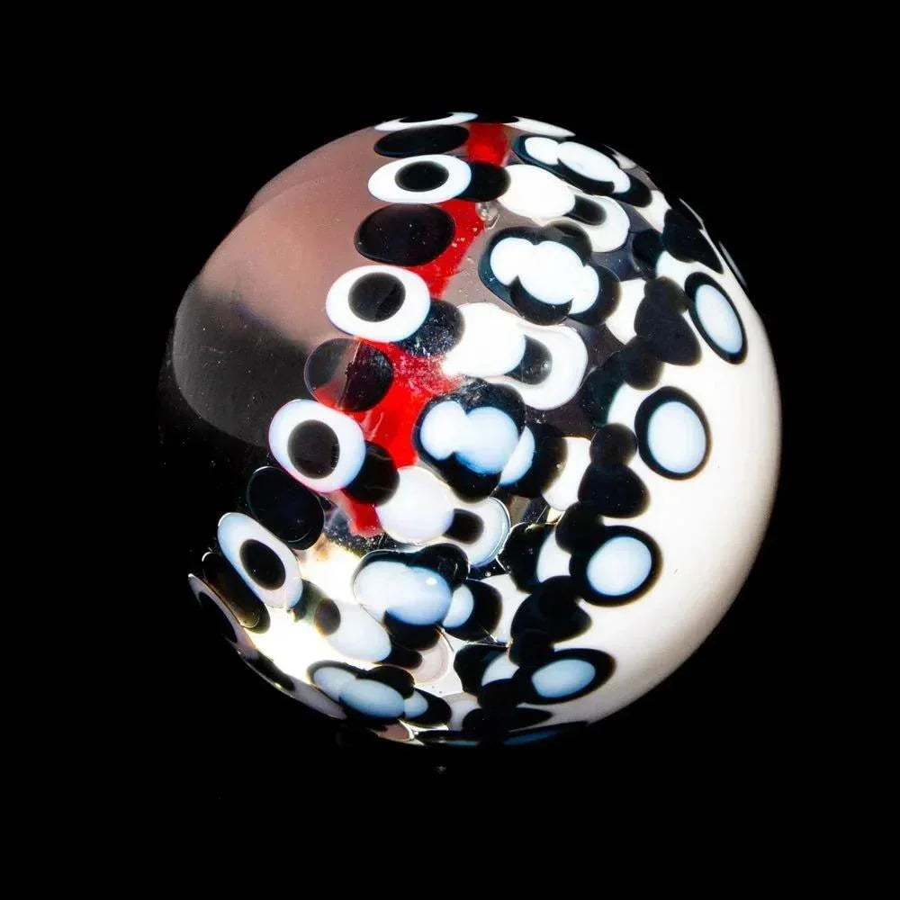 Handcrafted glass marble with black, white, and red abstract patterns on a dark background