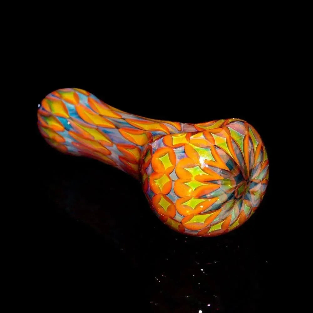 Handblown glass spoon pipe with vibrant orange, yellow, and blue geometric pattern on black background.