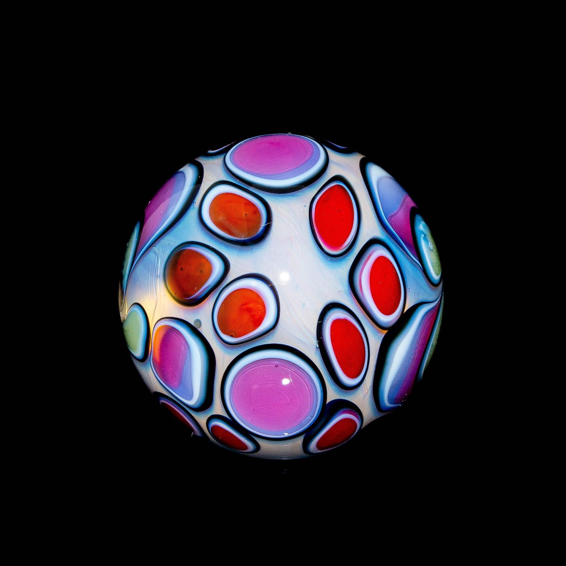 Colorful glass marble with pink, red, and orange pastel dot patterns on a black background