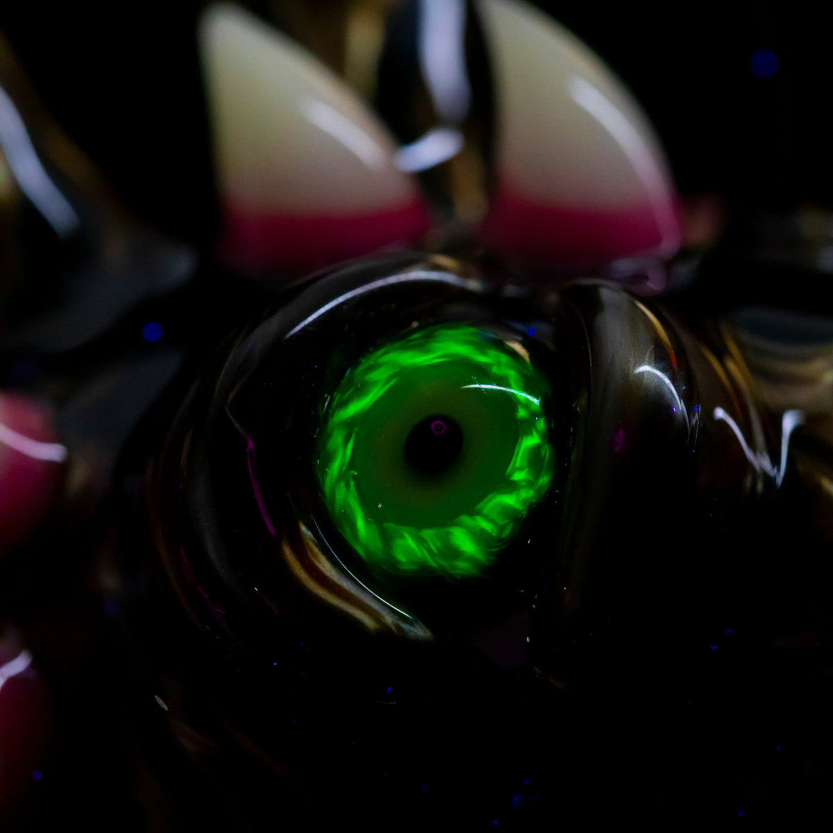 Close-up of hand-blown glass art with a glowing green eye and sculpted horn details