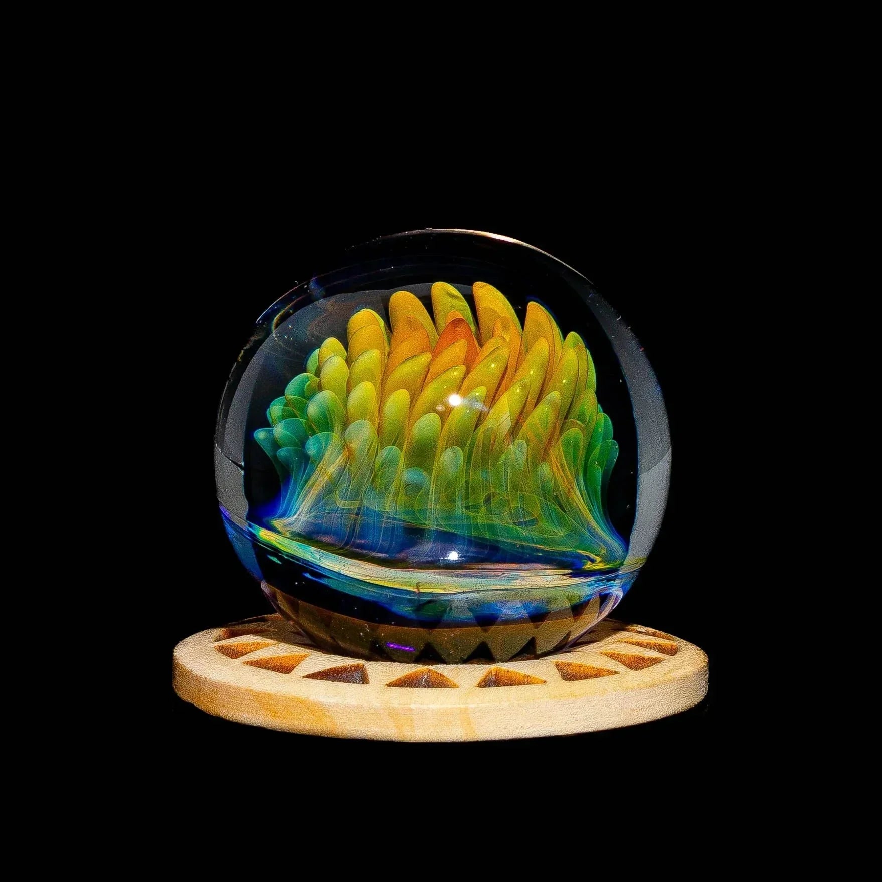 Handblown glass art marble with colorful flame pattern on a wooden display stand