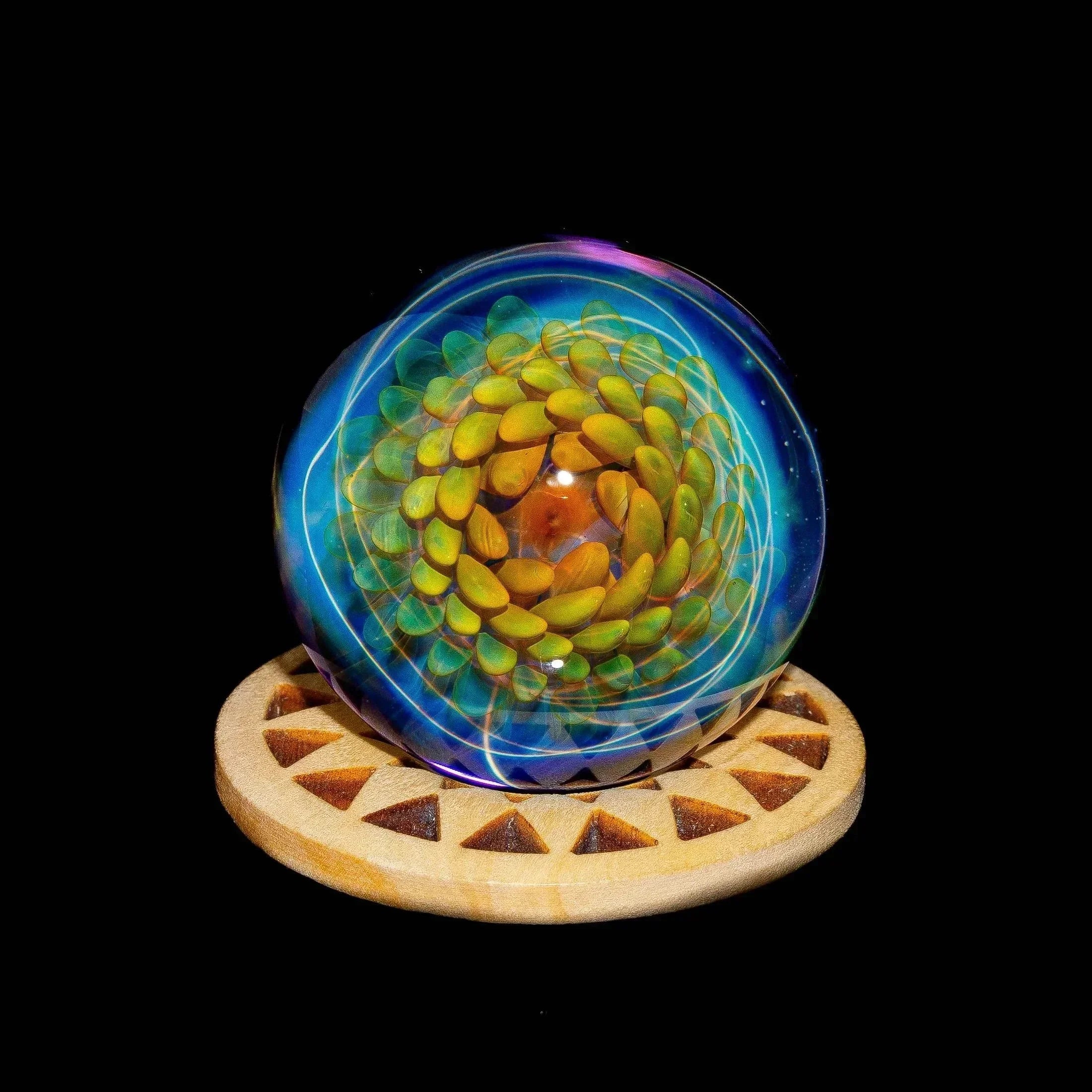 Intricate glass marble with yellow petals and blue swirls on a wooden display stand